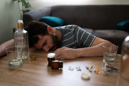 Drunk hispanic man passed out on the table surrounded with prescription pills and a bottle of...