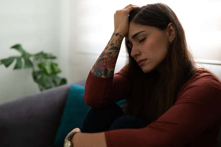Profile of an unhappy hispanic young woman sitting in his home sofa looking depressed and thinking...