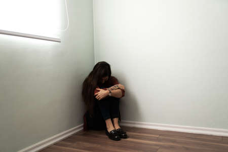 Young woman suffering from depression and loneliness sitting in a corner of the house. Latin woman...