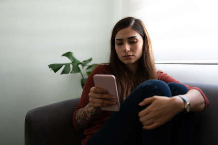 Beautiful and unhappy latin young woman using her smartphone looking sad and melancholic
