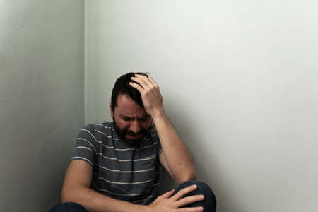 Sad hispanic man crying, sobbing and having an emotional breakdown in the floor. Adult man sitting alone in a house cornerの写真素材