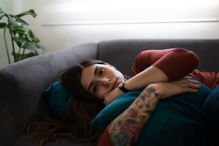 Portrait of a latin young woman lying on the couch and hugging a pillow. Woman in his 20s looking...