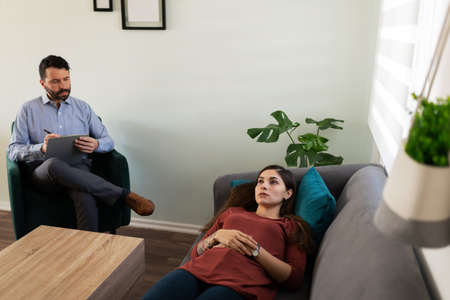 Depressed latin young woman lying on her psychiatrist's couch getting professional help because of her pshychological problemsの写真素材