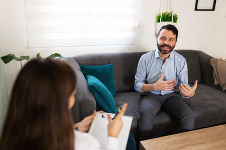 Latin man in his 30s talking about his feelings during a therapy session with her female psychiatrist about overcoming his depression problemsの写真素材