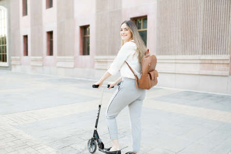 Attractive and happy caucasian female worker smiling and riding a scooter to commute to her workの写真素材