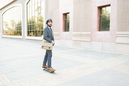 Professional male worker with a helmet looking peaceful and riding a skateboard en route to his...
