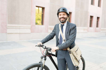 Happy latin man in his 30s wearing a business suit and a helmet. Worker riding a bike to get to his workplaceの写真素材