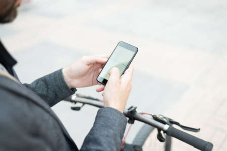 Close up of a businessman in an eco-friendly bike and checking the navigation map on his smartphone