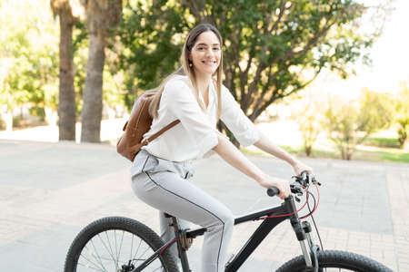 Happy businesswoman with a backpack riding a bike through a green park on her commute from office to homeの写真素材