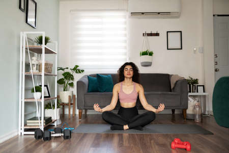 Young hispanic woman doing yoga exercises in the living room. Pretty woman in her 20s in an easy...