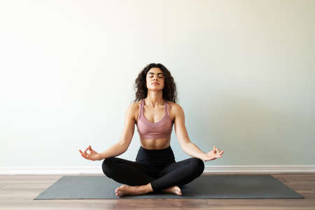 Attractive woman in her 20s doing an easy yoga pose in a mat. Young woman meditating in a mat, solid...