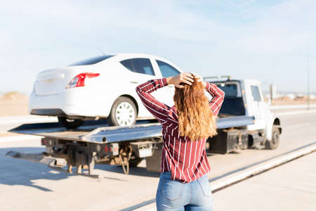 Young blond woman seen from behind looking upset with her hands in the head because her car is on a tow truckの写真素材
