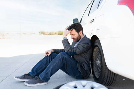Side view of a hispanic guy looking upset and waiting for road assistance to change his flat tireの写真素材