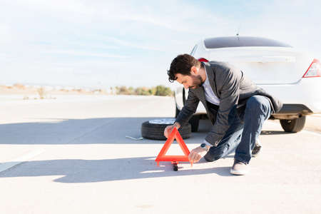Latin man placing the reflective triangle sign on the road as a warning because his car has a flat...