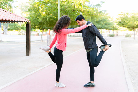 Healthy young couple doing warm-up exercises and stretching their legs before staring their morning...