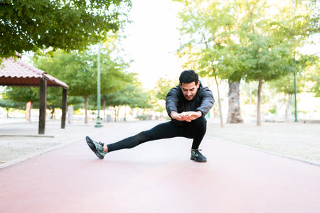 Athletic and handsome young man stretching his legs on the running track before starting his morning run in the parkの写真素材