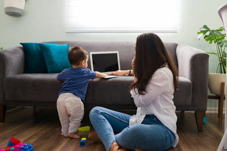 Young woman talking on phone and working on a laptop while her baby standing byの写真素材