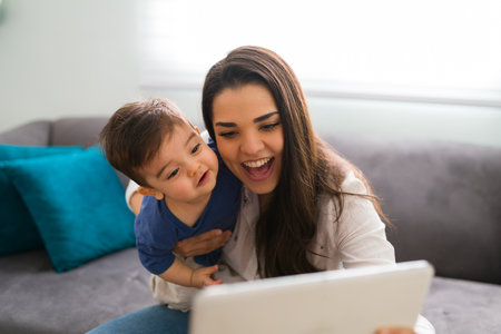Beautiful young caucasian woman and her little son sitting at home looking at digital tablet and...
