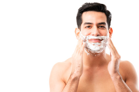 Portrait of a latin young man applying foam with hands to shave his beard against white backgroundの写真素材
