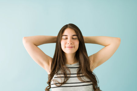 Young woman with beautiful hair, her eyes closed and her arms behind her head with a dreamy expression against a blue backgroundの写真素材