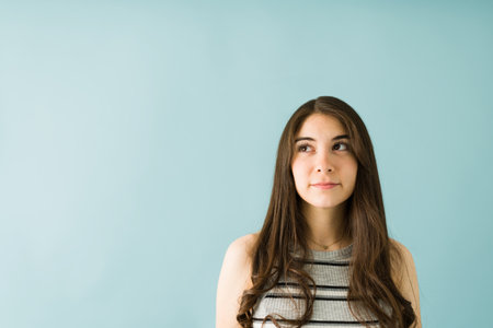 Pretty woman in her 20s looking up and thinking about something creative, isolated against a blue background with copyspaceの写真素材
