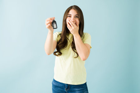 Caucasian woman in her 20s can't believe she got her first car. Young woman holding the keys of her...