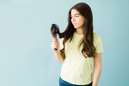 Pretty woman in her 20s is brushing her long and damaged hair and is upset because it got tangled in the hair brushの写真素材