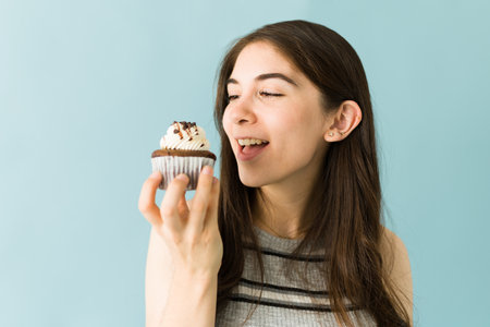 Profile of an attractive young woman about to eat a chocolate cupcake. Woman isolated against a blue backgroundの写真素材