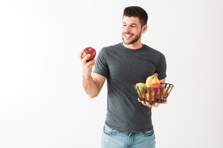 Hispanic young man is smiling and playing with an apple. Attractive man holding a basket of fresh fruits, isolated against a white backgroundの写真素材