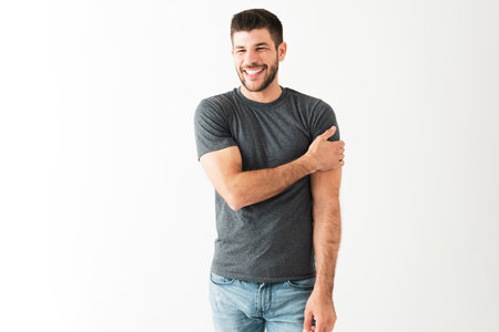 Attractive latin man in his 20s with a big smile is laughing with someone and standing in front of a...