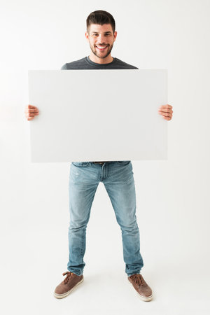Latin young guy smiling and looking happy while holding a white blank sign against a white backgroundの写真素材