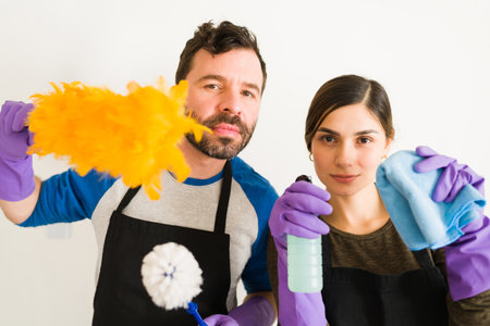Closeup of Hispanic couple holding a feather duster and other cleaning products and getting ready...