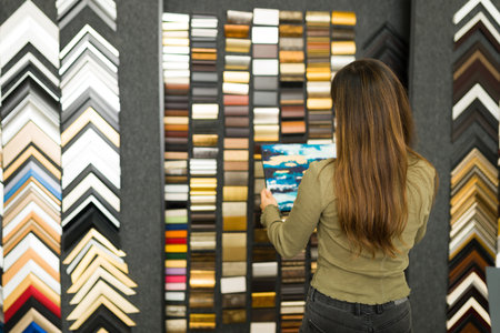 Young woman seen from behind on a store is choosing a wood frame to buy for her new canvas