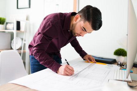 Handsome young man with a determined look is designing and drawing a blueprint at his desk for a new architectural projectの写真素材