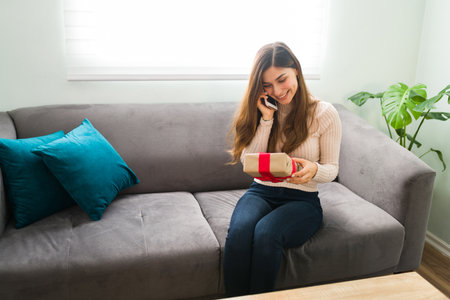 Happy woman in her 20s is talking with her partner on the phone to thank him for the gift he send her home for their romantic anniversaryの写真素材