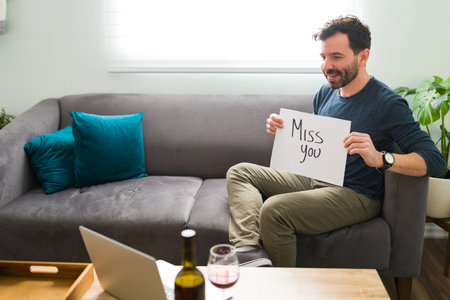 Good-looking latin man in his 30s is showing his long-distance partner or girlfriend a miss you card...