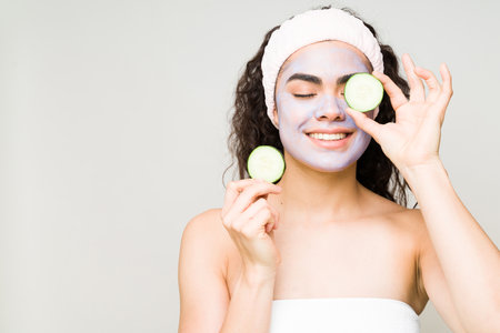 Attractive female model enjoying a day at the beauty spa. Young woman with a facial treatment holding some cucumber slicesの写真素材