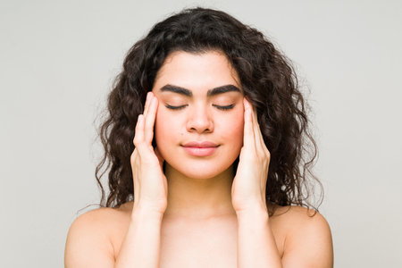 Relaxed young woman touching her temples with her eyes closed. Beauty and skin care model showing her flawless faceの写真素材