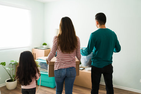 Husband, wife and little girl holding boxes in the living room to start unpacking their furniture and unloading household goods during moving dayの写真素材
