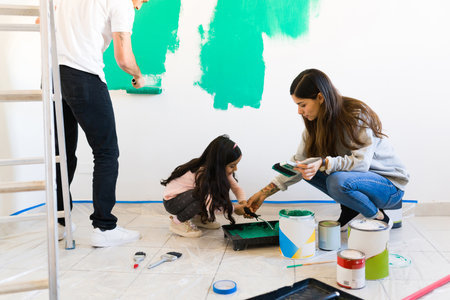 Young woman helping a little girl to put paint on a roller to start painting and redecorating the walls of their new bedroomの写真素材