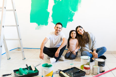 Young woman, man and girl doing a home renovation. Smiling and happy familiy looking at the camera while sitting on the floorの写真素材