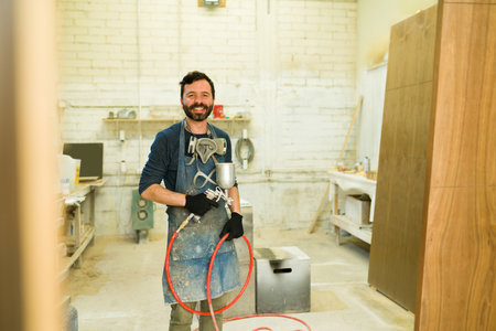 Portrait of an attractive man with respirators holding a spray gun. Happy male carpenter in a paint...
