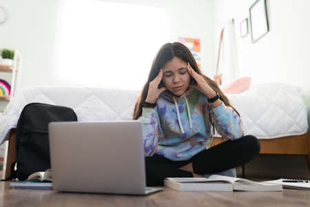 Stressed female student feeling overwhelmed while studying for her school exams in her bedroom. Worried adolescent girl does not understand and having trouble with her homeworkの写真素材