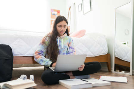 Cute adolescent girl typing a school essay on her laptop computer. Focused teenager girl doing online research for her homeworkの写真素材