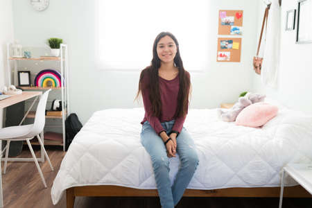 Caucasian teenager girl smiling and sitting on a beautiful bed. Portrait of an adolescent showing off her bedroom with girly decorationsの写真素材