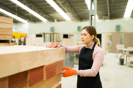 Attractive female worker standing next to a pile of wooden boards. Female carpenter doing her job at...