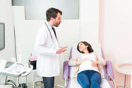 Handsome male gynecologist telling a pregnant woman in pain to start doing breathing exercises to...