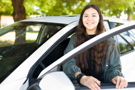 Cute teenage girl getting into the driver's seat of her car and smiling. Adolescent girl going out...