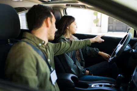 Young man giving instructions and directions to a teenage girl during her driving lessons. Male instructor talking to an adolescent inside a carの写真素材