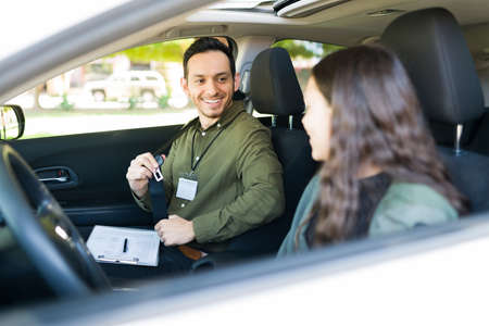 Happy male instructor smiling and teaching a teenage girl student to drive. Adolescent girl feeling...